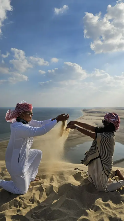 Two guides throwing handfuls of sand into the wind on the dunes