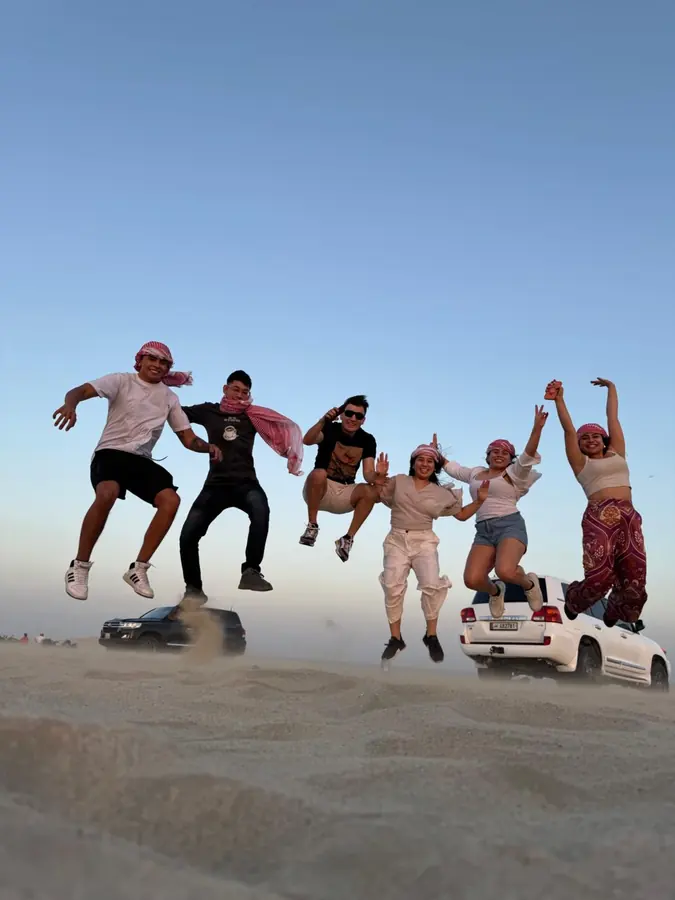 Guests leaping with sandboards on the crest of a dune